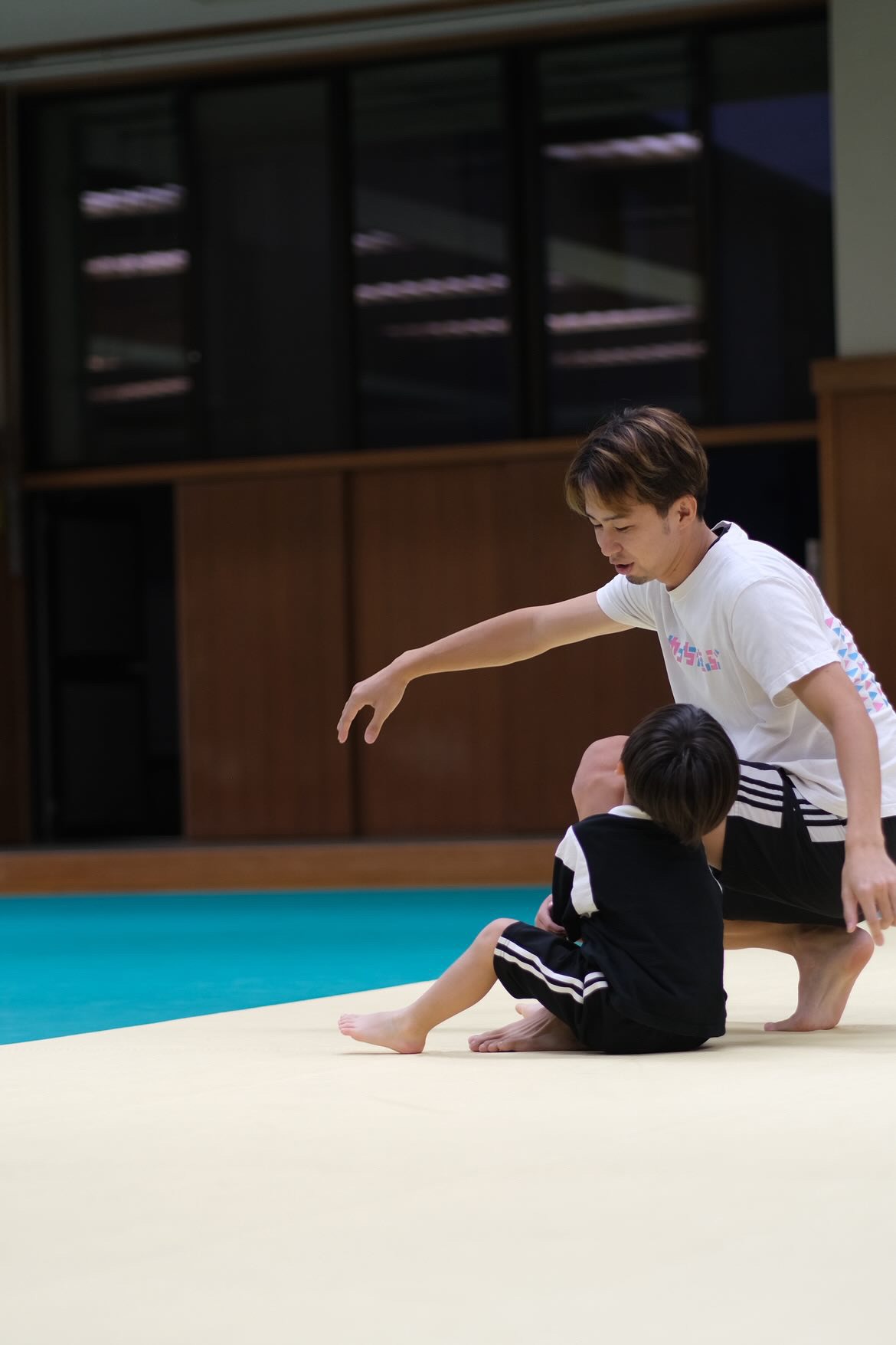 畳に座りこんだこどもの横で、指導者が手を差し出したまま待っている