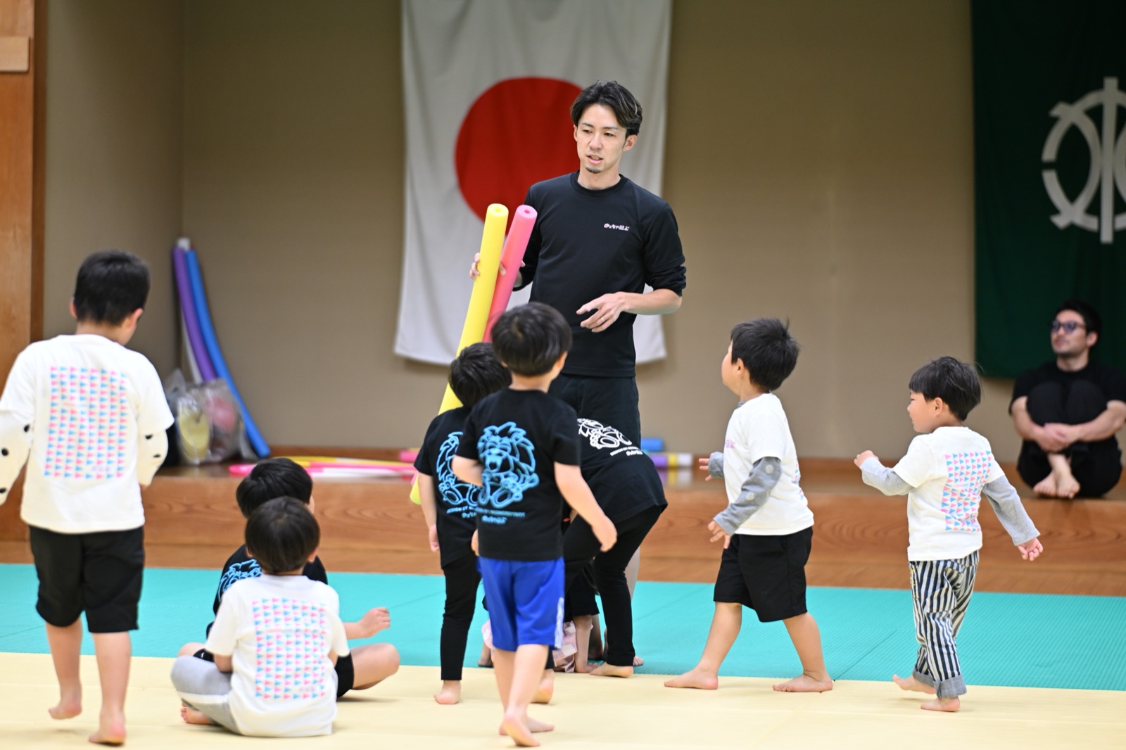 道場で、棒を持った先生をこどもたちが取り囲んでいる
